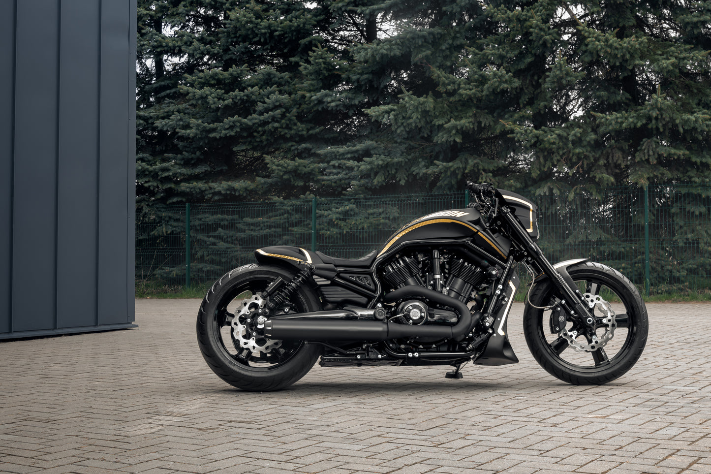 Harley Davidson motorcycle with Killer Custom V-Rod seat for "Short/Smooth Oval" rear fenders from the side, outside in front of the garage with some trees in the background