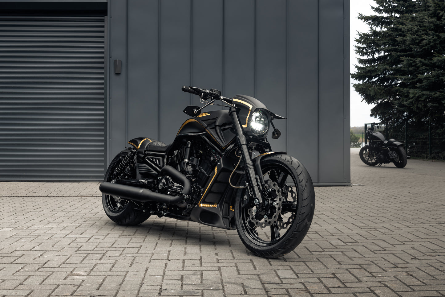 Harley Davidson motorcycle with Killer Custom "Aggressor" V-Rod headlight fairing from the side in front of the modern garage with some trees and another motorcycle in the background