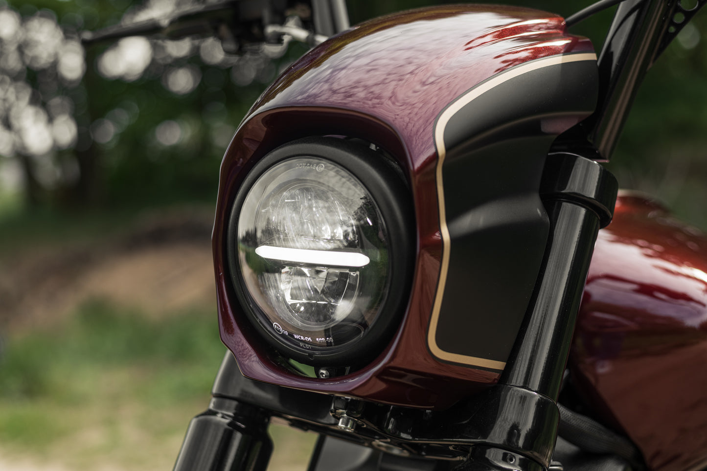 Zoomed Harley Davidson motorcycle with Killer Custom "Tomahawk" series headlight fairing from the front with a blurry forest background