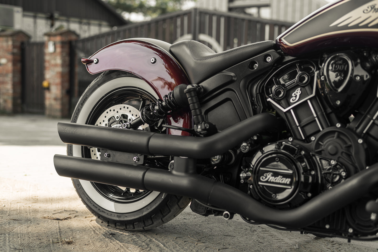 Zoomed Harley Davidson motorcycle with Killer Custom "Apache II" rear fender from the side with a fence and the gates in the background