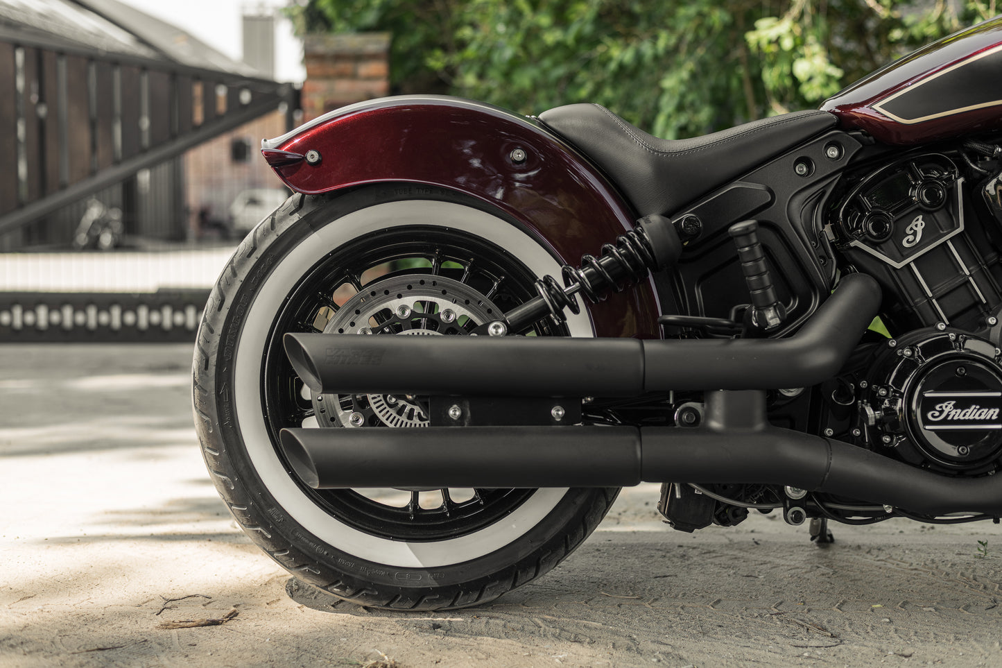 Harley Davidson motorcycle with Killer Custom Indian scout solo seat from the side with the gates and some trees in the background