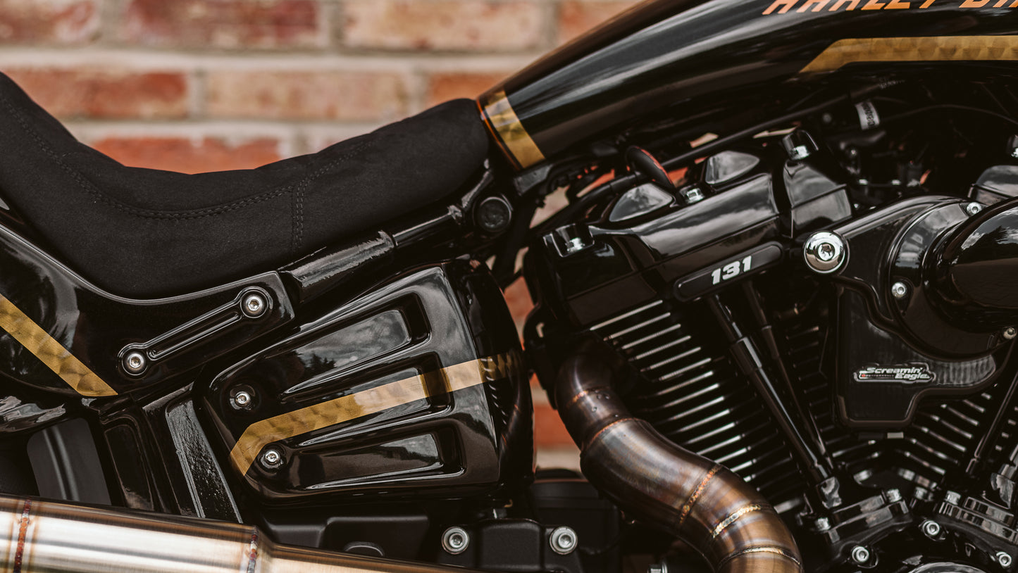 Zoomed Harley Davidson motorcycle with Killer Custom rear shock upper bolt covers from the side with a brick wall in the background