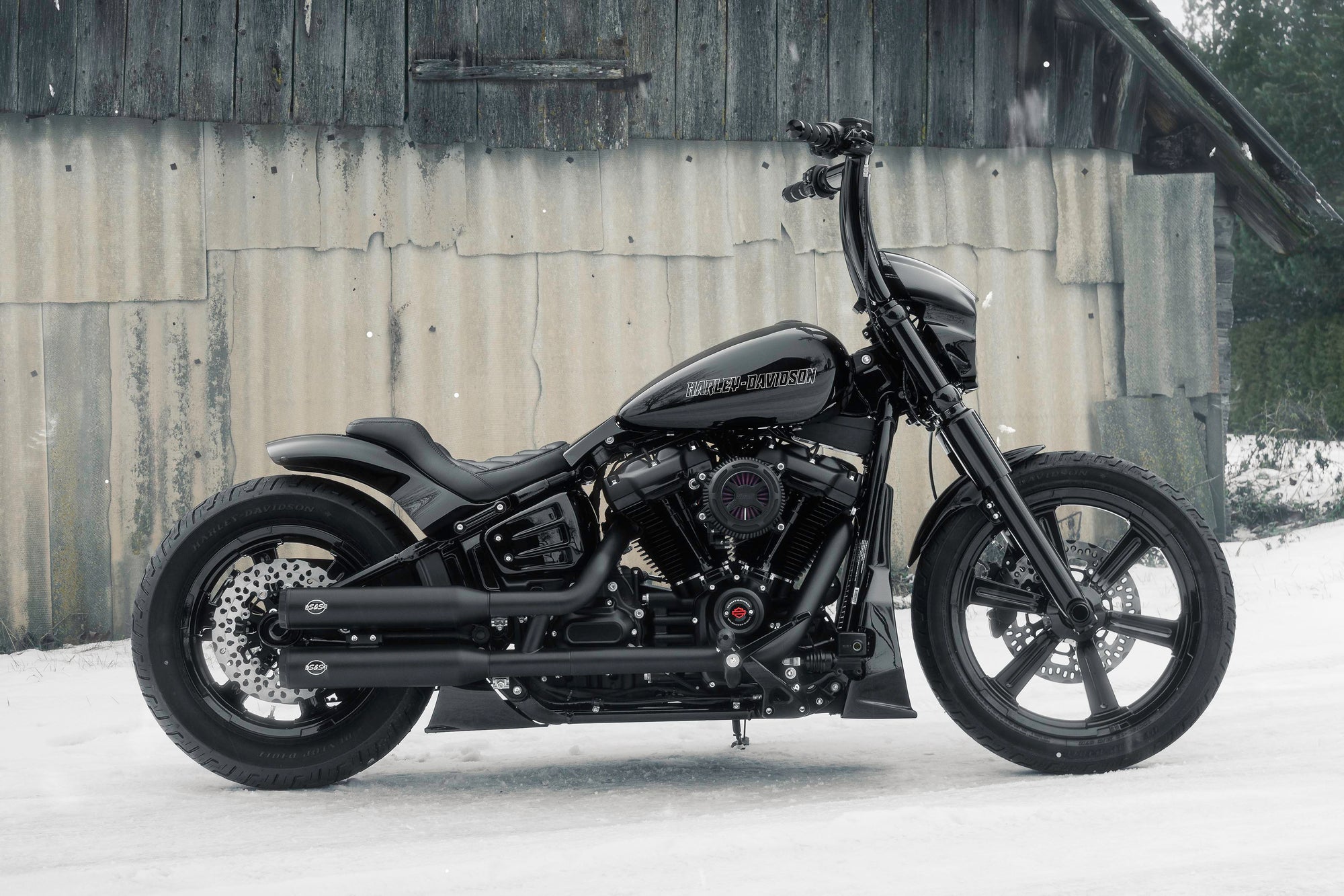 Modified Harley Davidson Softail motorcycle with Killer Custom parts from the side outside on a snowy day with an abandoned shack in the background