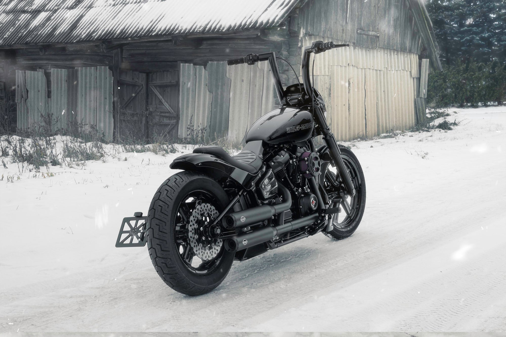 Harley Davidson motorcycle with Killer Custom parts from the rear outside on a snowy day with an abandoned shack in the background