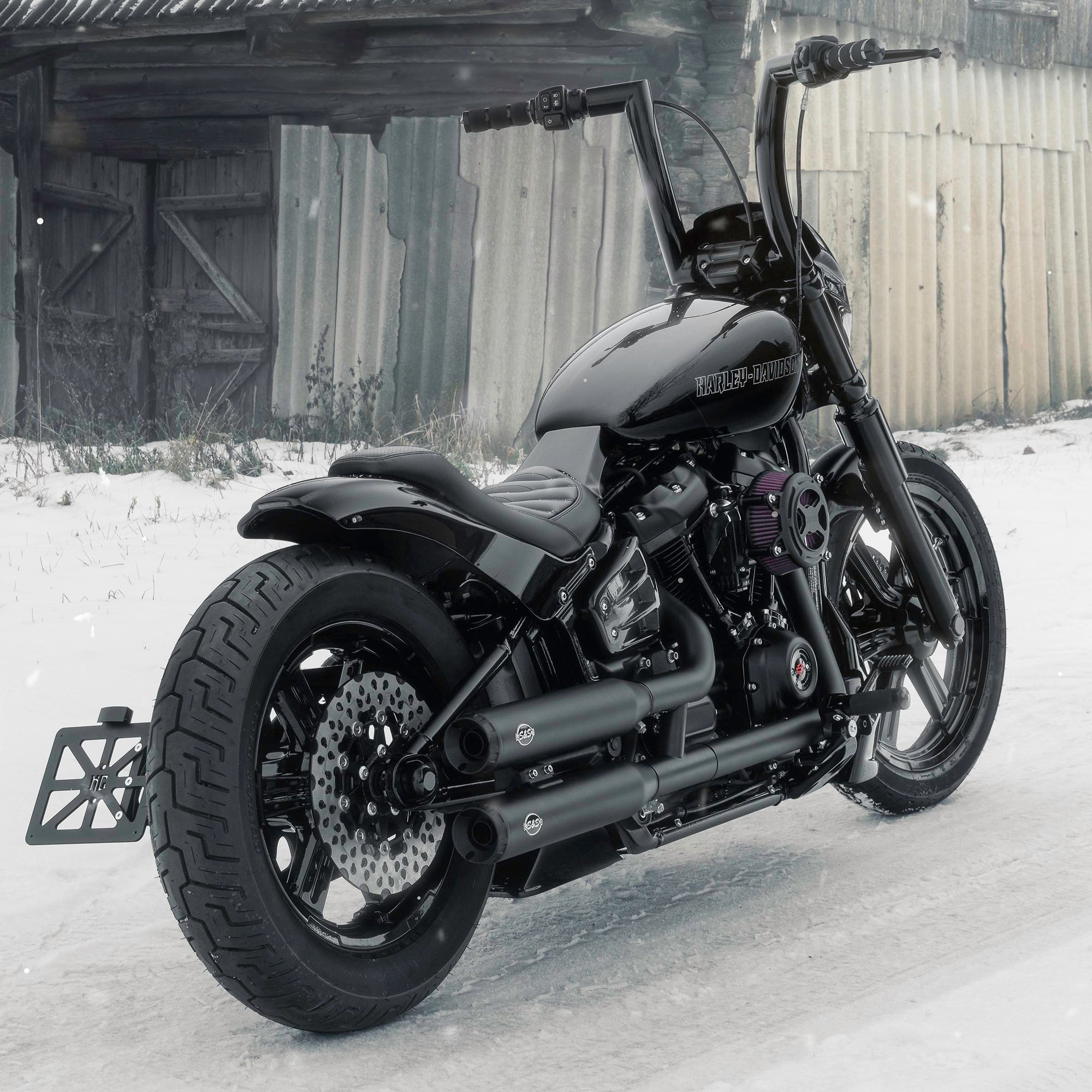 Harley Davidson motorcycle with Killer Custom parts form the rear outside on a snowy day with an abandoned shack in the background