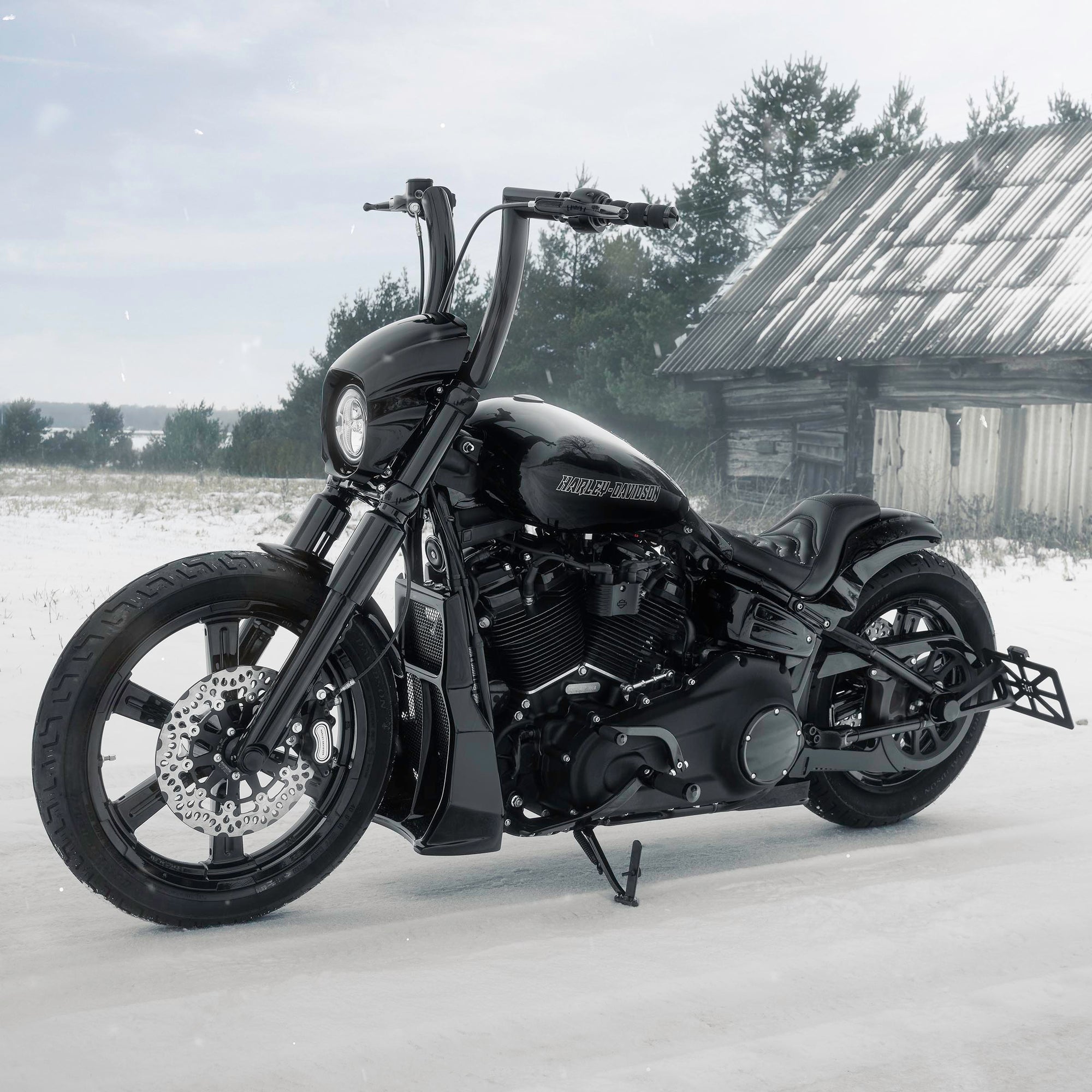 Modified Harley Davidson Softail motorcycle with Killer Custom parts from the side outside on a gloomy winter day with an abandoned shack in the background