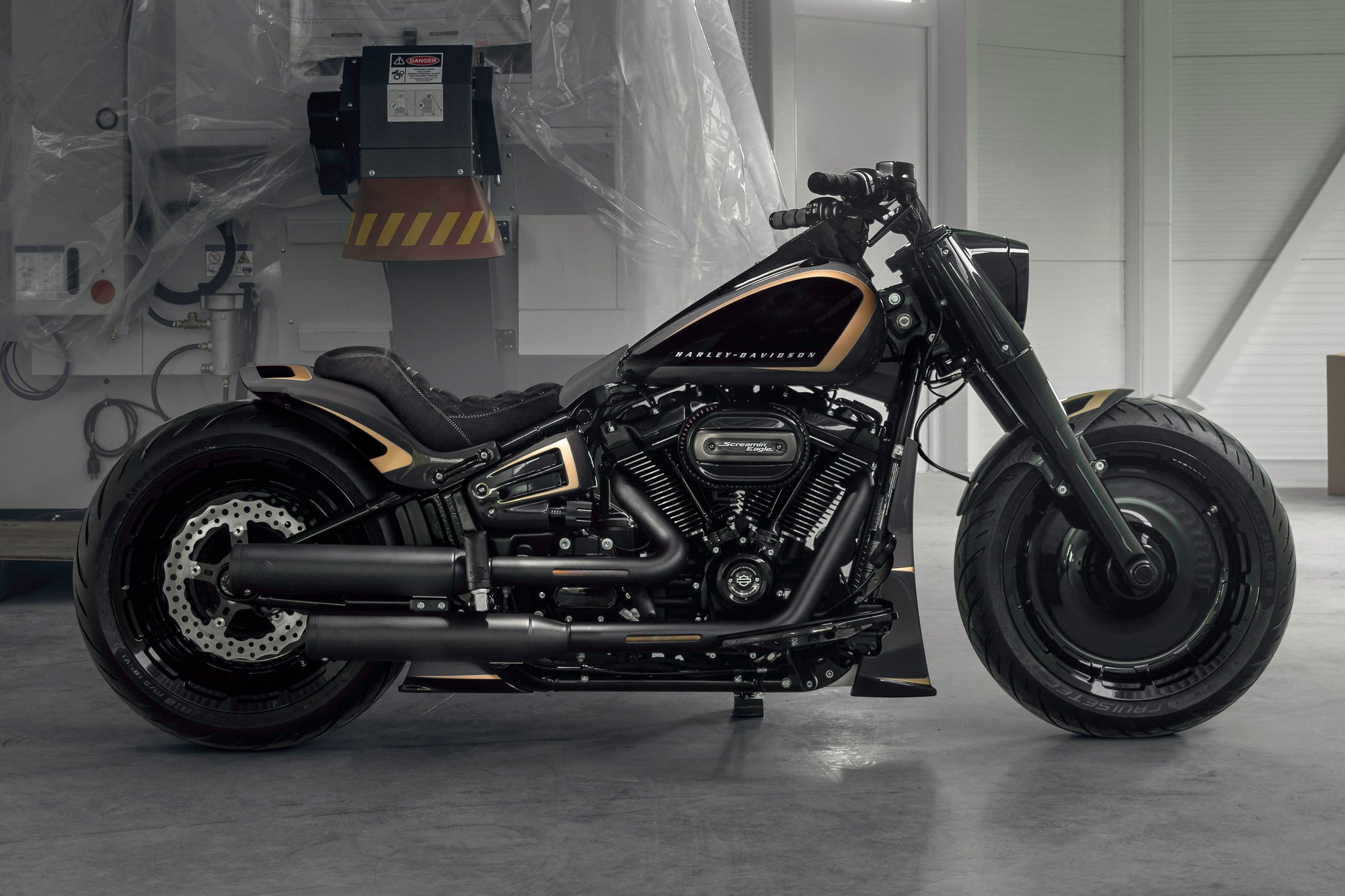 Modified Harley Davidson Fat Boy motorcycle with Killer Custom parts from the side in a modern garage with some equipment in the background