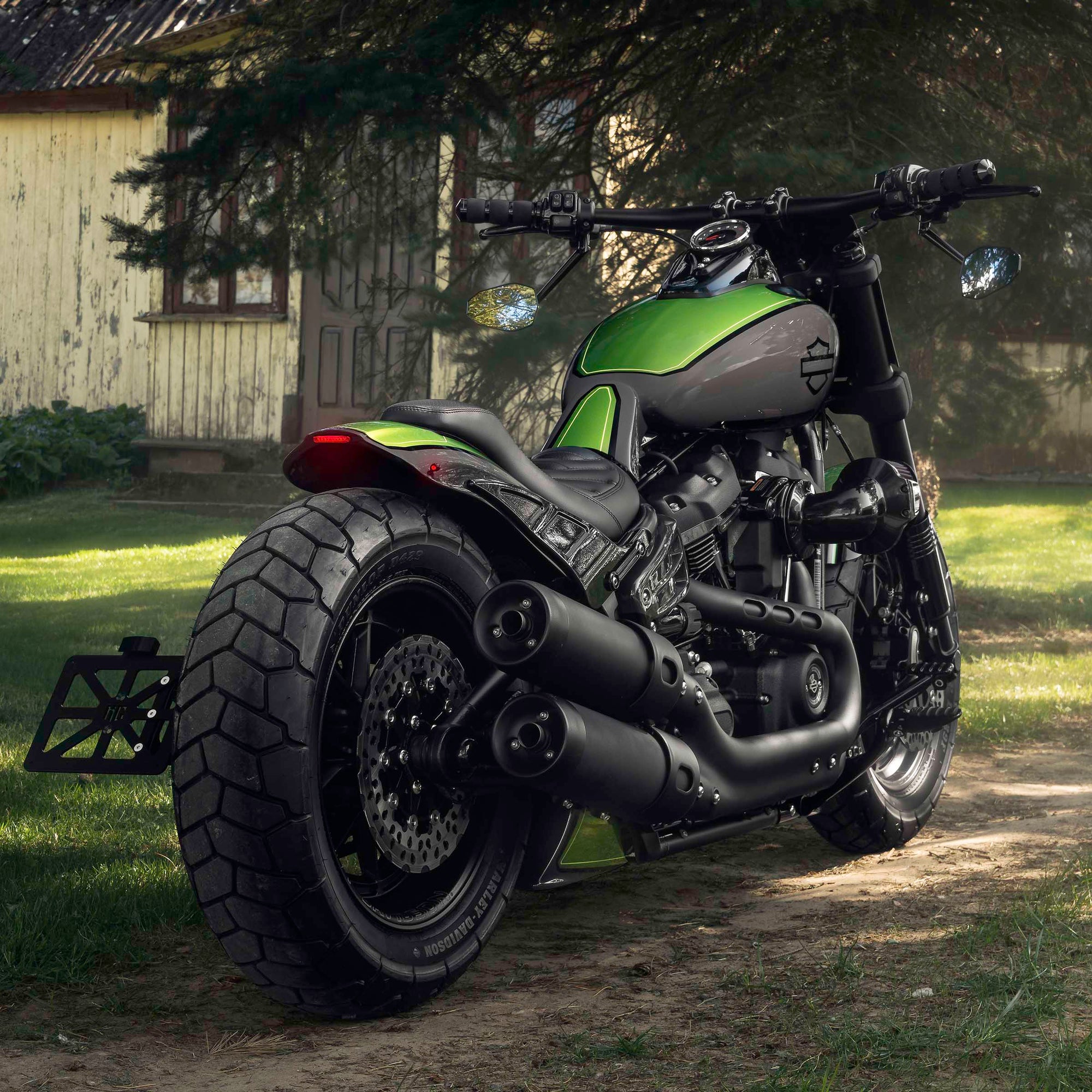 Modified Harley Davidson Fat Bob motorcycle with Killer Custom parts from the side with some trees and the country house in the background