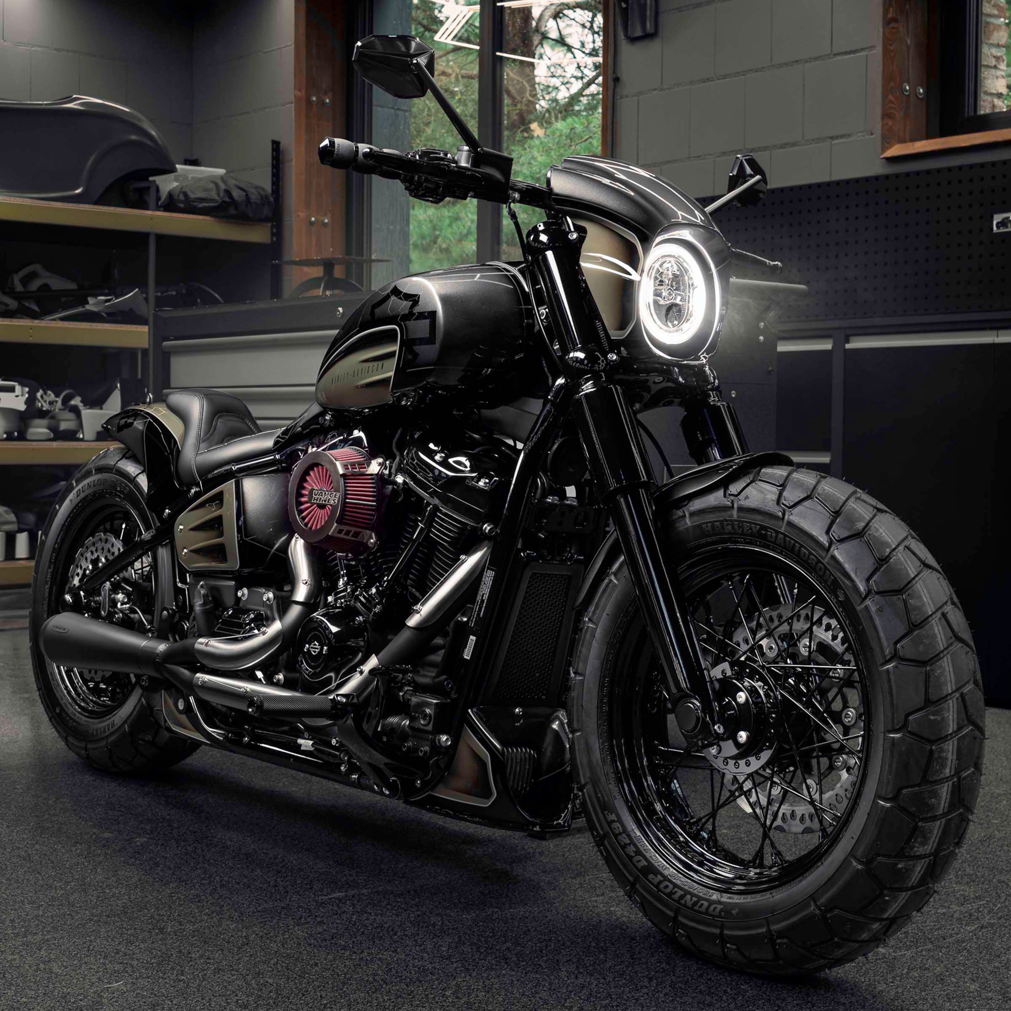 Modified Harley Davidson Street Bob motorcycle with Killer Custom parts from the front with some garage equipment and a window in the background