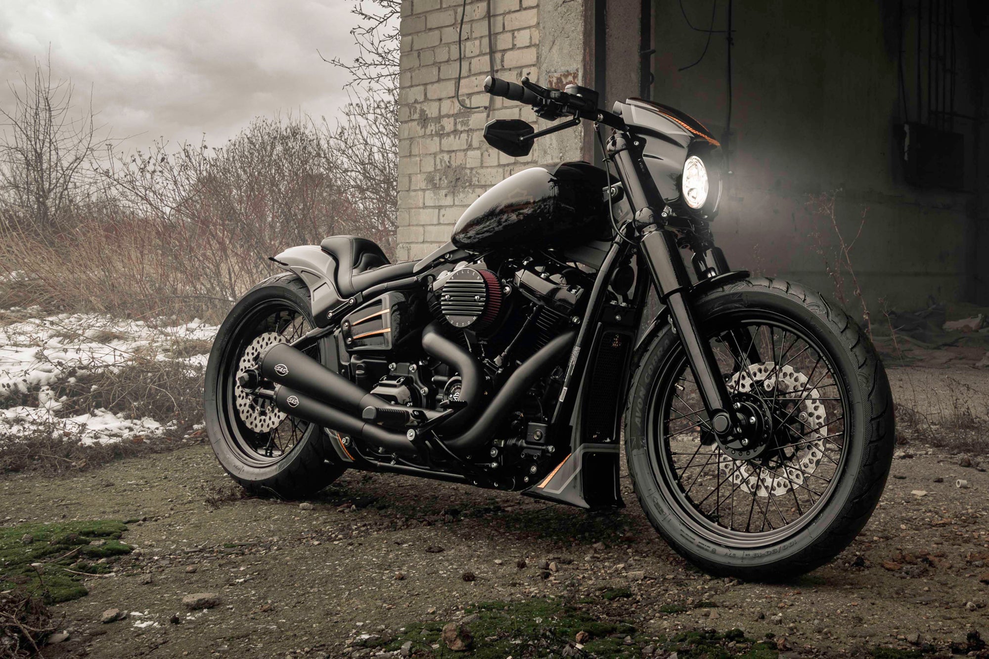 Modified Harley Davidson Street Bob motorcycle with Killer Custom parts from the side outside in an abandoned environment with some snow in the background