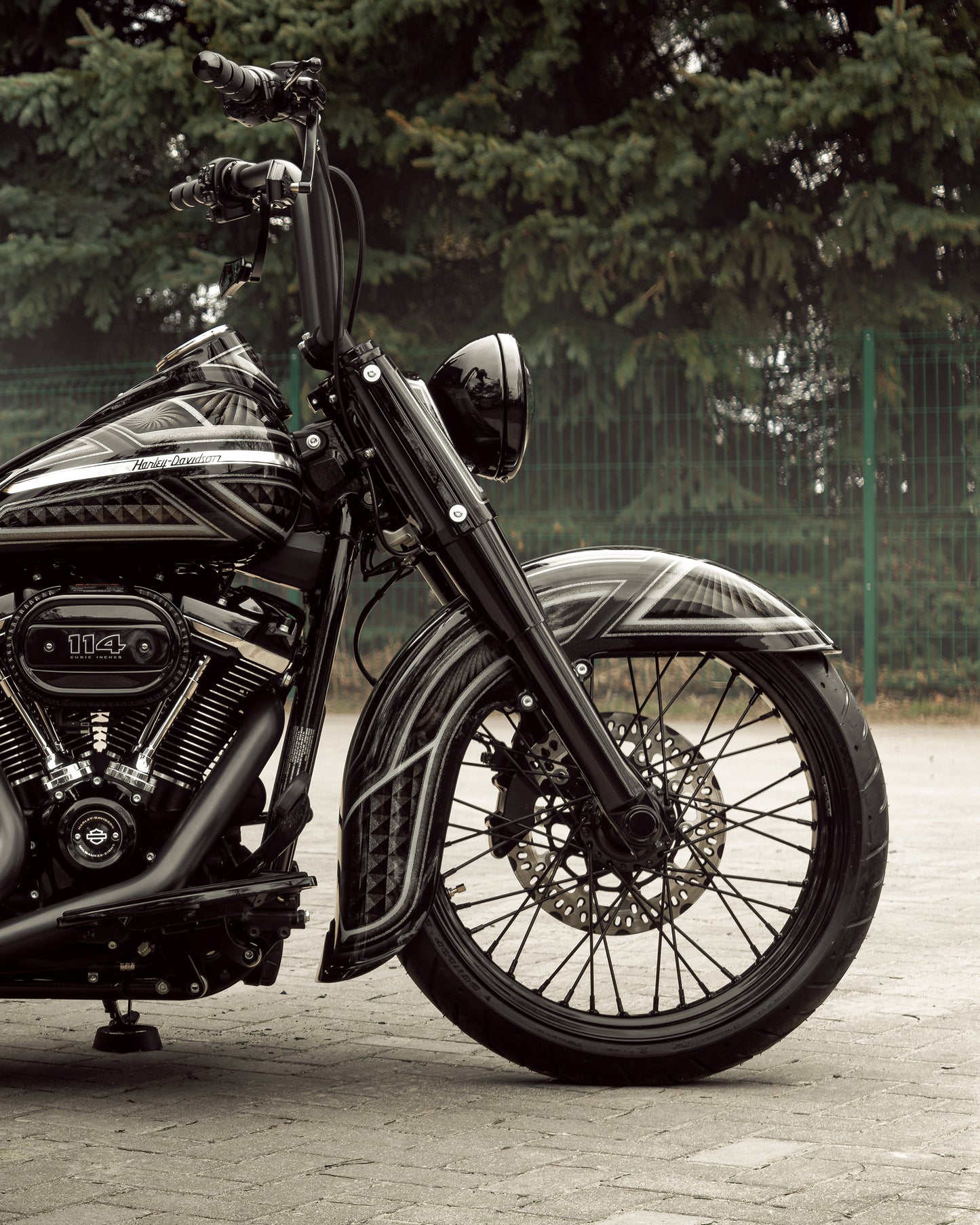 Zoomed Harley Davidson motorcycle with Killer Custom "Classic" fender for front wheel from the side outside with some trees and a fence in the background