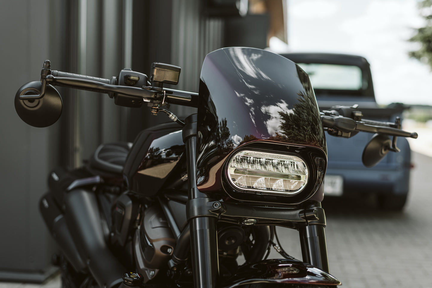 Harley Davidson motorcycle with Killer Custom Harley Davidson "Road Warrior" headlight fairing mask from the front outside on a sunny day with blurred car in the background