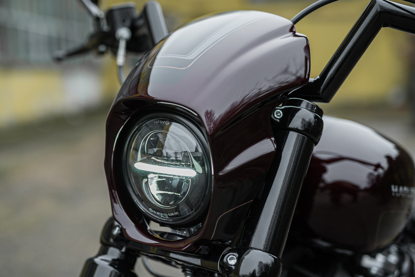 Zoomed Harley Davidson motorcycle with Killer Custom Headlight ECE approved with parking light from the front with a blurry aged wall in the background