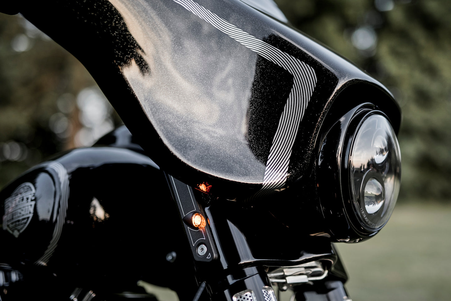 Zoomed Harley Davidson motorcycle with Killer Custom front LED turn signals from the side with blurry trees in the background