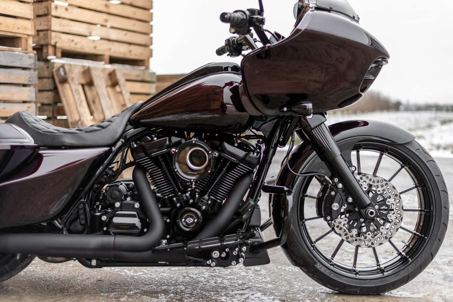 Harley Davidson motorcycle with Killer Custom front fender from the side with visible snow and some wooden pallets in the background
