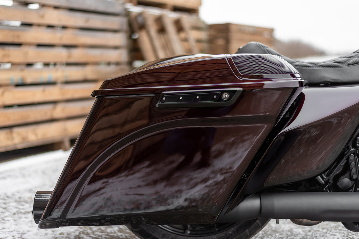 Zoomed Harley Davidson motorcycle with Killer Custom saddlebag latch hinge inserts from the side with wooden pallets and visible snow in the background