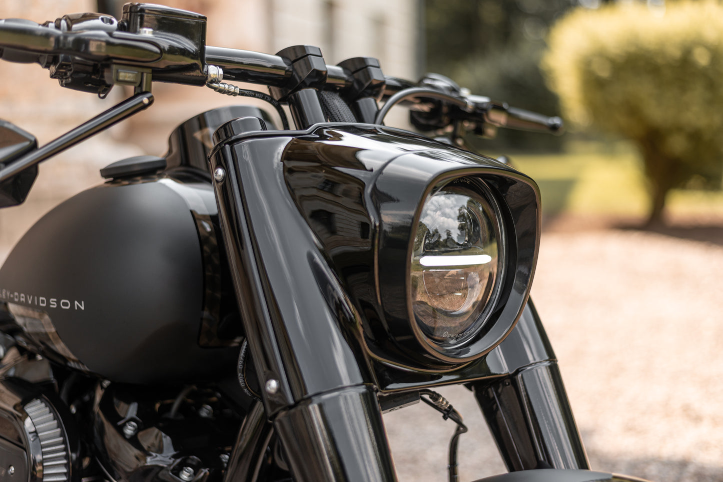 Zoomed Harley Davidson motorcycle with Killer Custom riser set for handlebar from the front outside on a sunny day with some blurred trees in the background