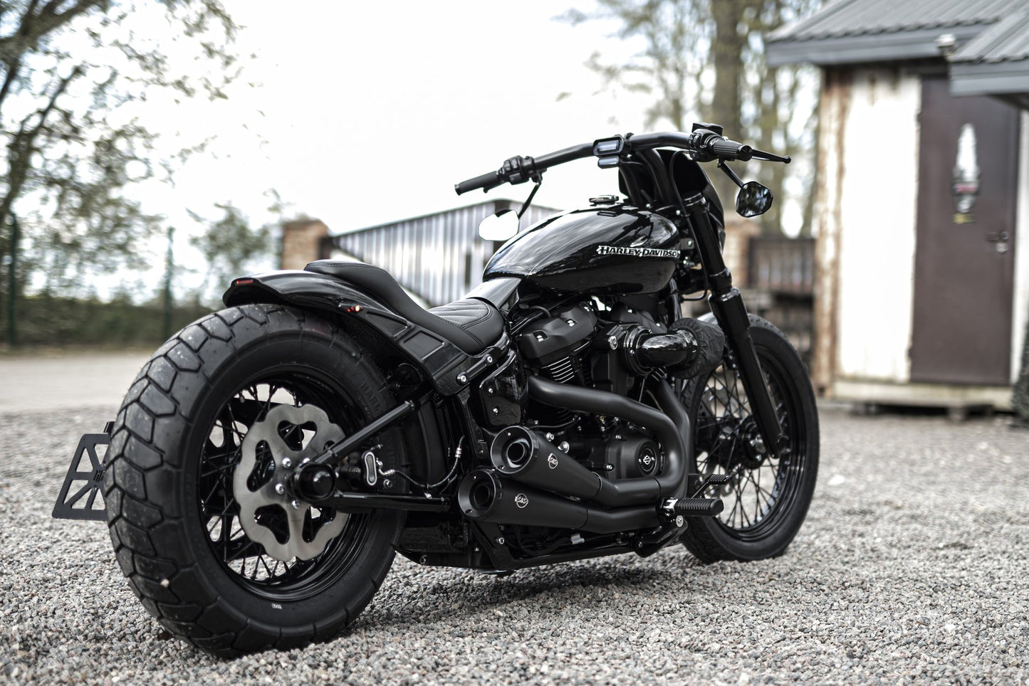 Harley davidson motorcycle with Killer Custom "Bobbstr" rear fender from the side outside in front of the house blurry background