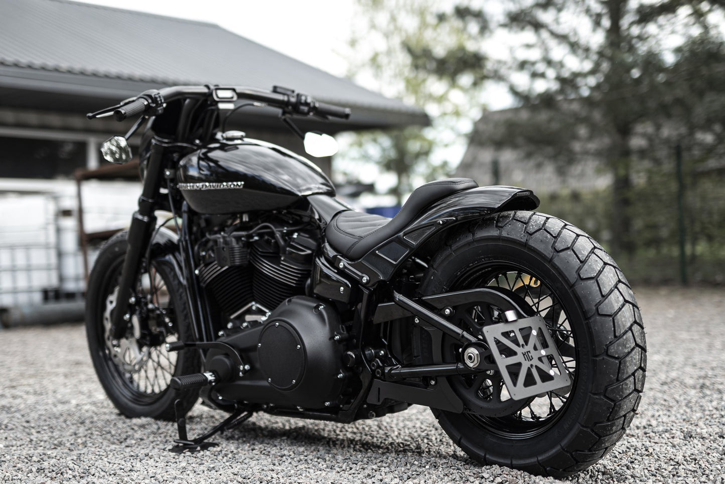 Harley Davidson motorcycle with "Bobbstr" rear fender from the side by Killer Custom in the yard blurry background